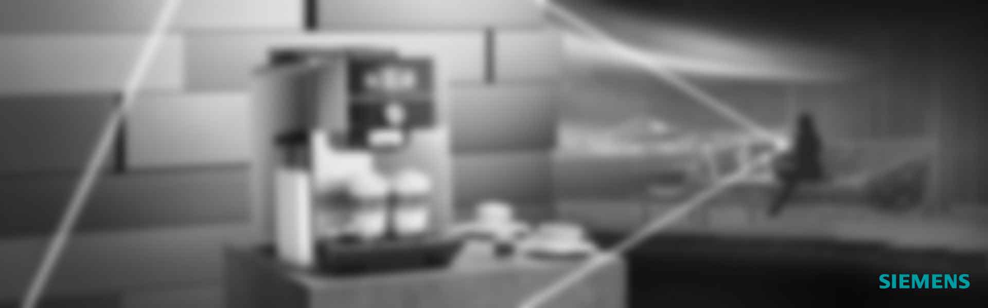 Eine Person steuert mit dem Smartphone einen Kaffeevollautomaten, im Hintergrund steht die Kaffeemaschine auf einer Theke.